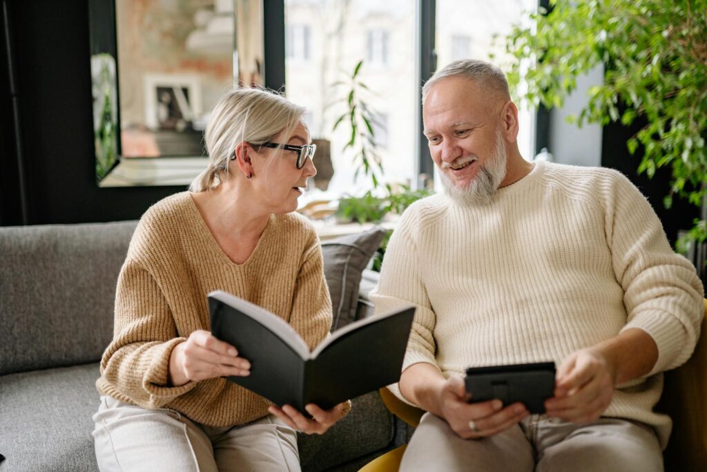 Smiling elderly couple reading and relaxing on a cozy sofa indoors.
