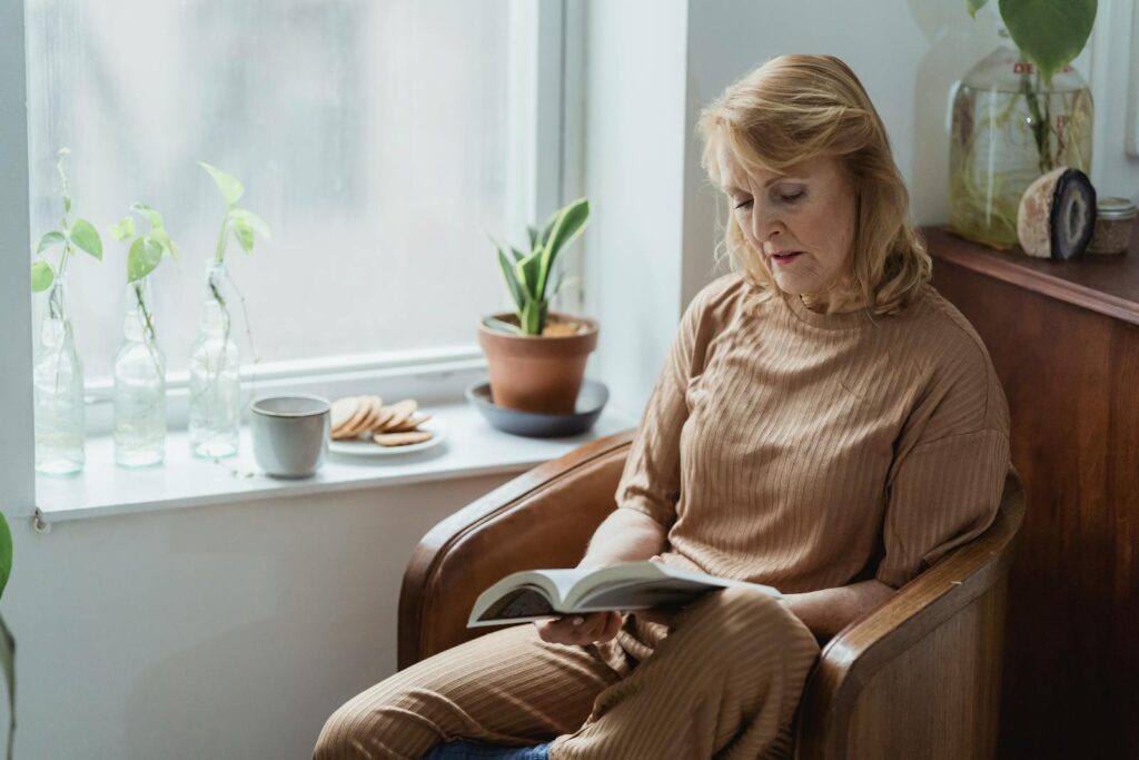 Senior woman enjoying a peaceful reading moment by the window in a cozy armchair.