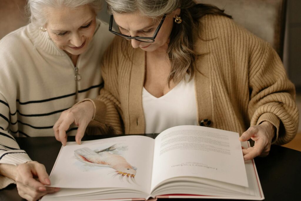 Two elderly women reading an illustrated book, sharing a moment of connection.