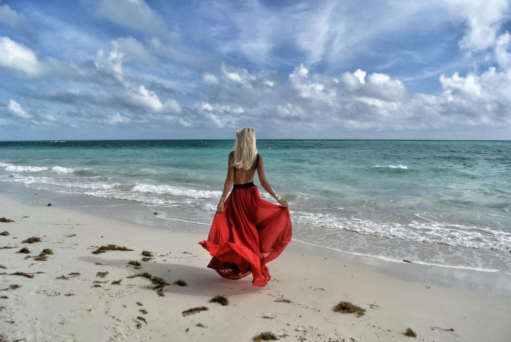A woman in a flowing red dress enjoys a walk on a scenic Bahamas beach.