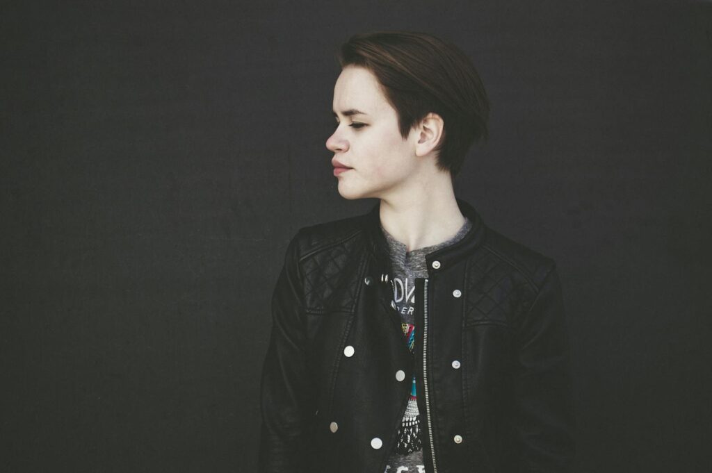 A stylish young woman poses in a black leather jacket against a dark background.