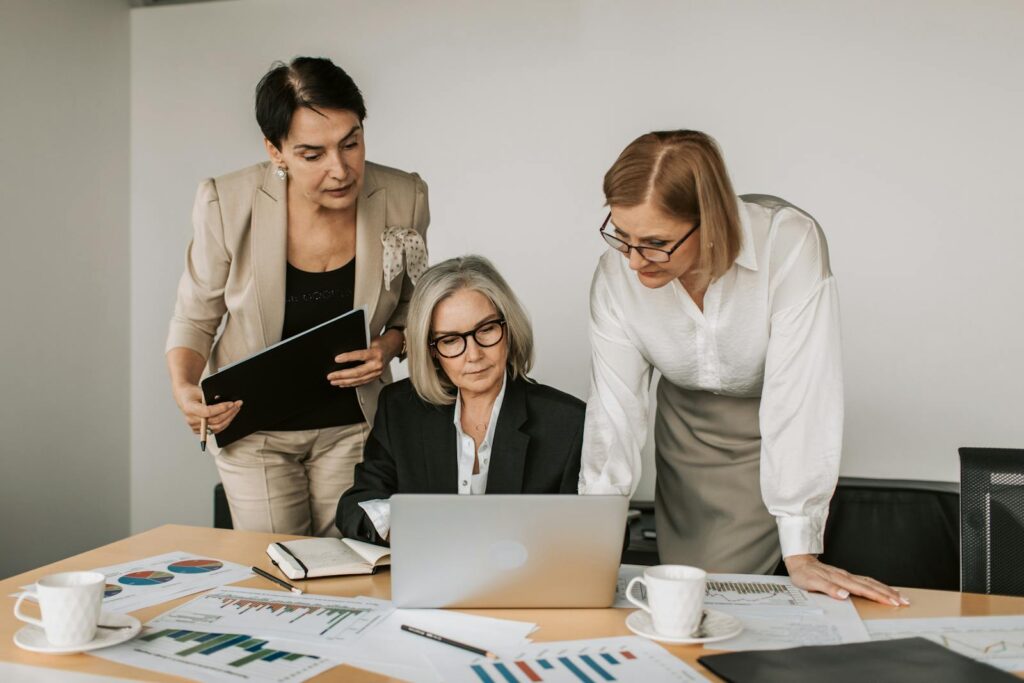 Three women in a business meeting, discussing strategy with charts and laptop.