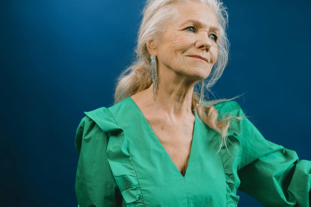 Portrait of an elegant elderly woman in a green dress against a blue background.