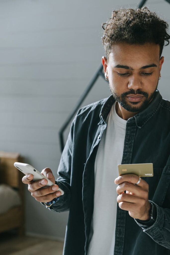 A young man using his smartphone and credit card for online shopping indoors.