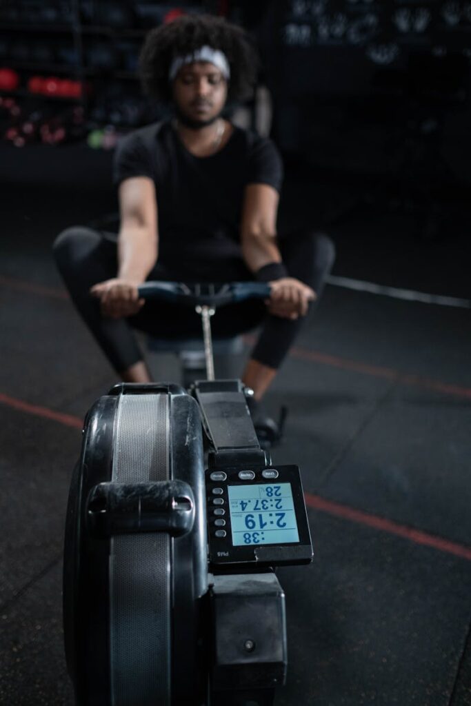 A focused man exercising on a rowing machine in a dimly lit gym setting, emphasizing physical fitness.