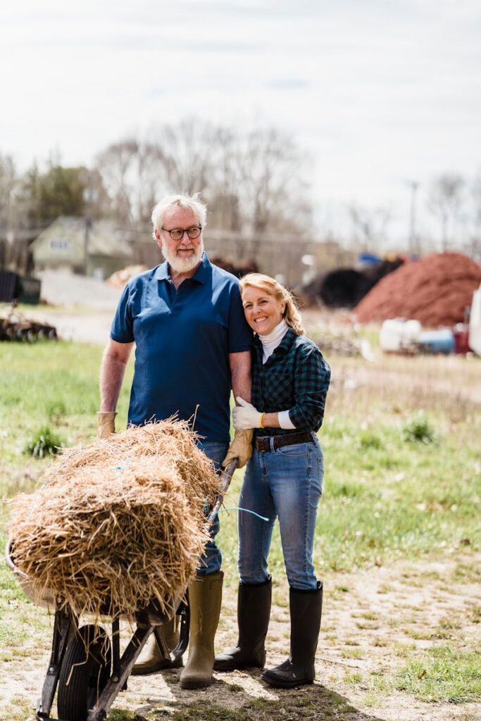 Elderly couple enjoying gardening with a wheelbarrow filled with hay outdoors.