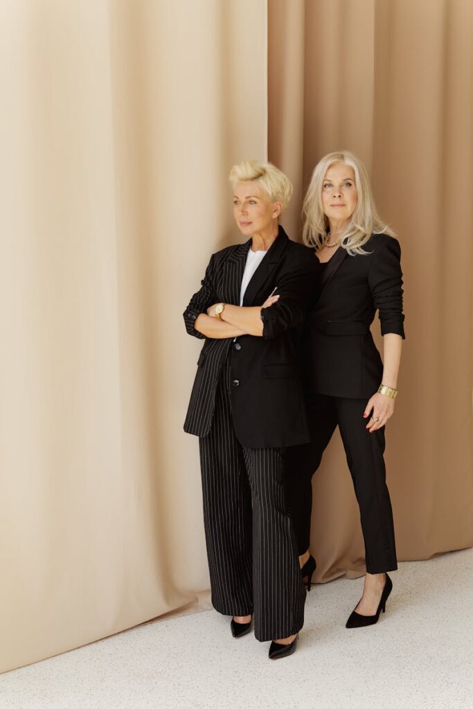 Stylish senior women in black attire posing elegantly indoors, showcasing fashion.