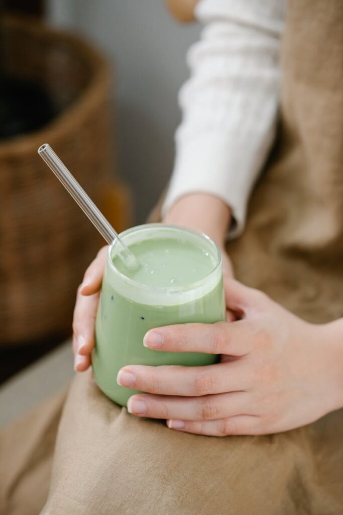 A green smoothie in a glass being held by a woman, emphasizing healthy living.