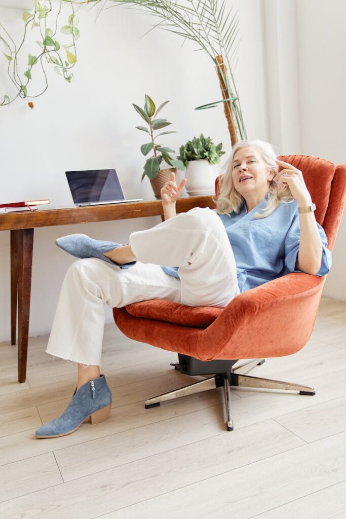 A senior woman smiling and relaxing in a modern home office chair surrounded by plants.