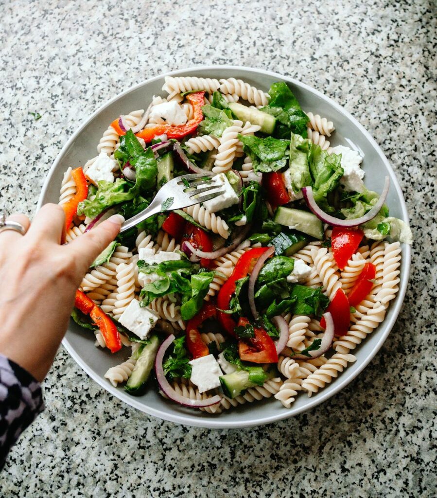 Vibrant pasta salad with fresh vegetables and feta cheese, captured from above.