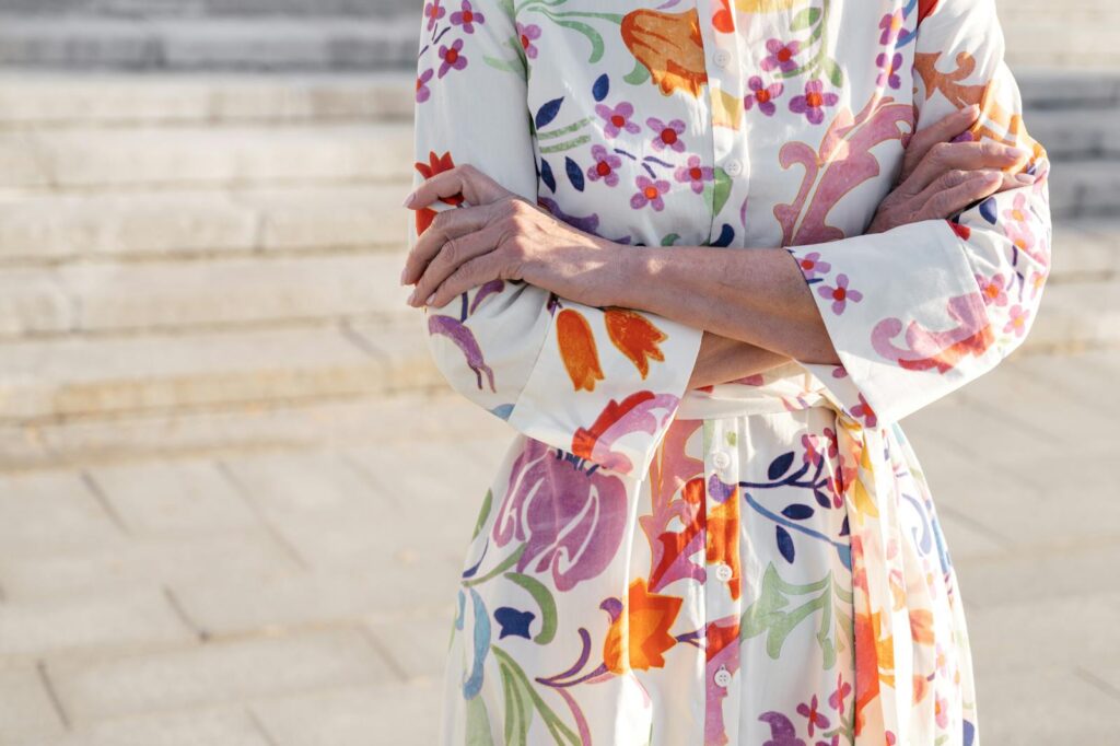 Senior woman in a colorful floral dress enjoying a sunny day outdoors with arms crossed.