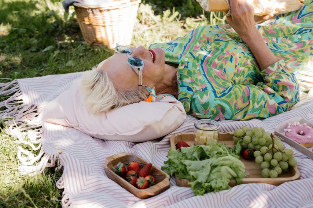 Elderly woman relaxing with picnic items on a sunny day, showcasing joy and leisure.