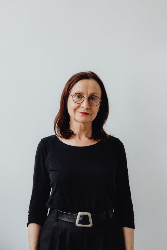 Elegant portrait of a senior woman in black attire, smiling softly indoors against a light gray background.