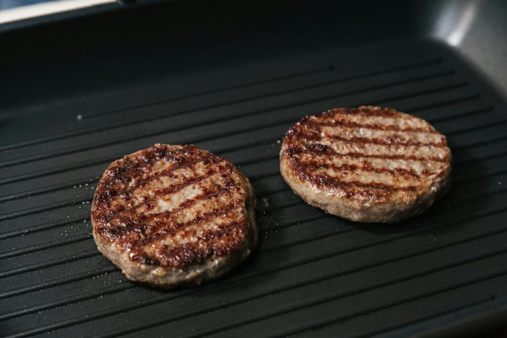Close-up of juicy grilled beef patties cooking on a flat iron skillet.
