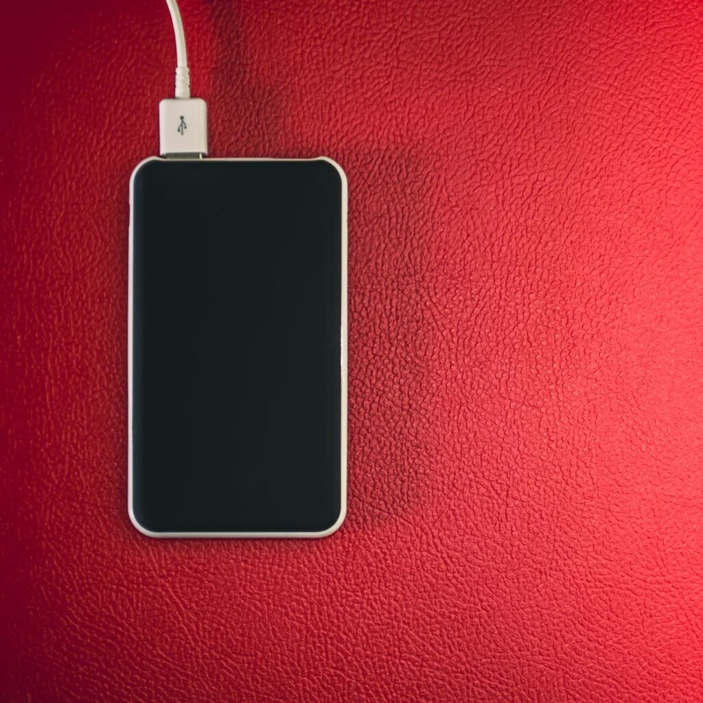 A smartphone connected to a charger placed on a red leather surface.
