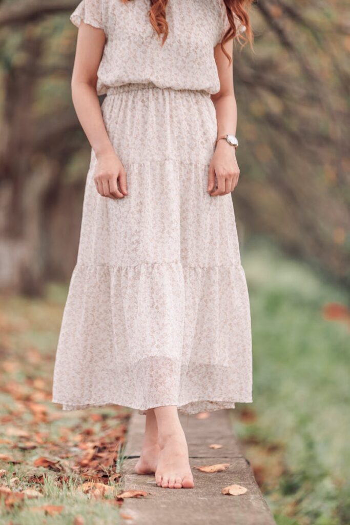 A woman in a floral dress stands barefoot in a scenic park, embodying grace and tranquility.