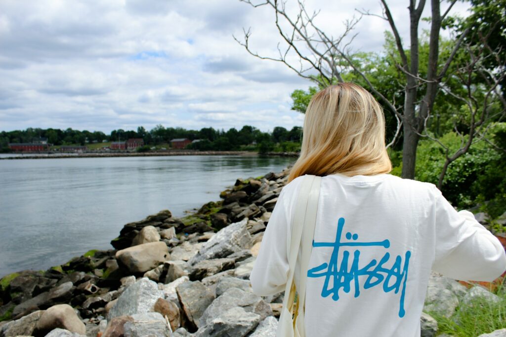 woman in white and blue shirt standing on rocky shore during daytime