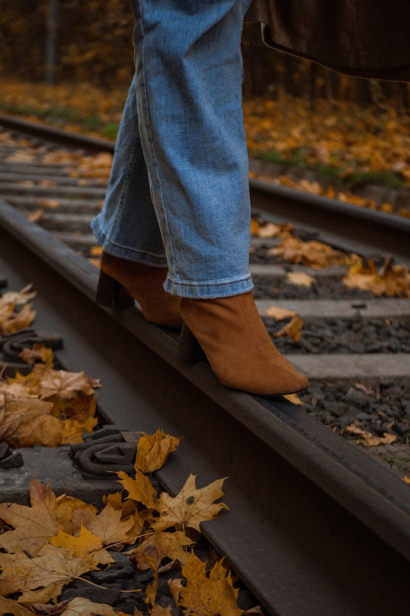 A person standing on a train track with leaves on the ground