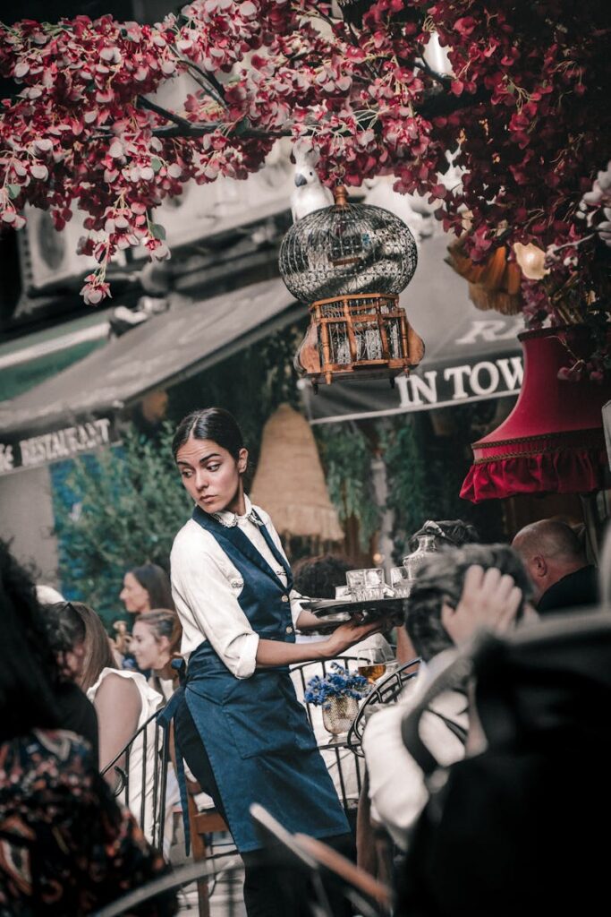 Waitress in blue apron serving drinks at a bustling outdoor cafe in Athens, Greece.
