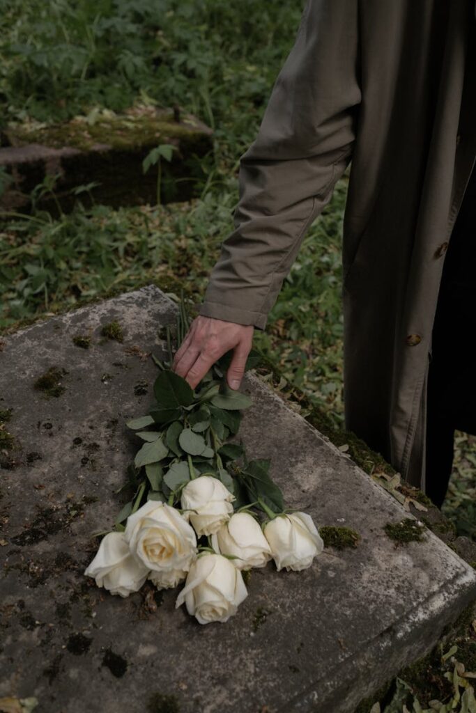 A solemn moment captured as a hand places white roses on a moss-covered tombstone, symbolizing loss and bereavement.