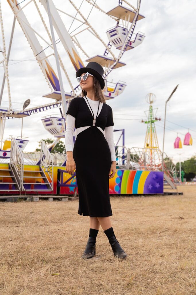 Fashionable woman in hat and dress poses at a colorful fairground.