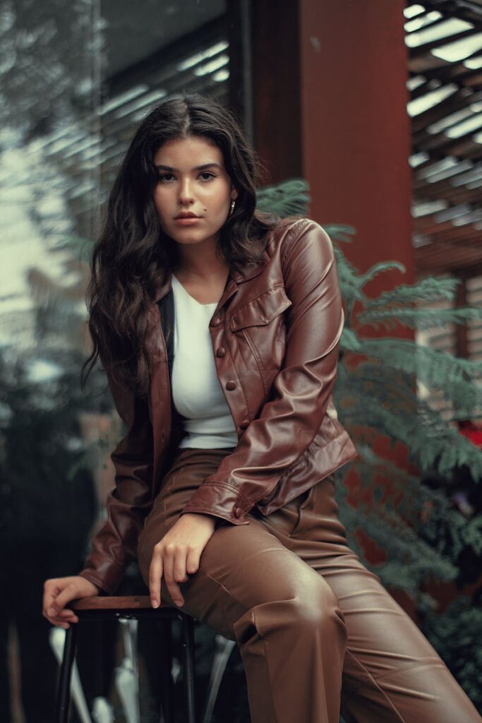 Stylish woman in brown leather outfit sitting on a stool outdoors in SP, Brazil.