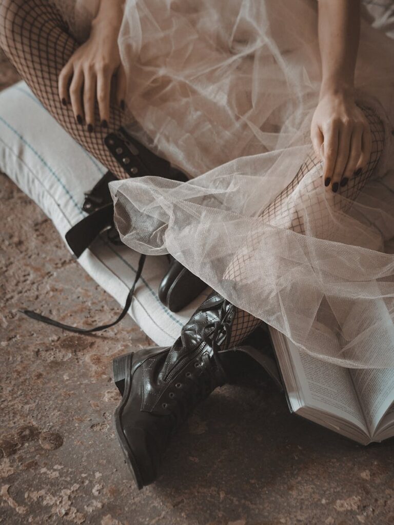 Fashionable woman in fishnet stockings and leather boots, sitting on cushions, evoking a vintage and moody style.