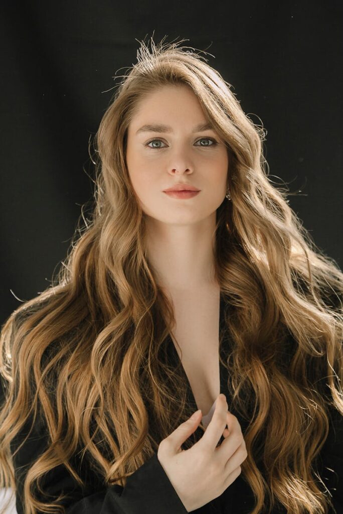 Close-up portrait of a young woman with long, wavy blonde hair against a black background.