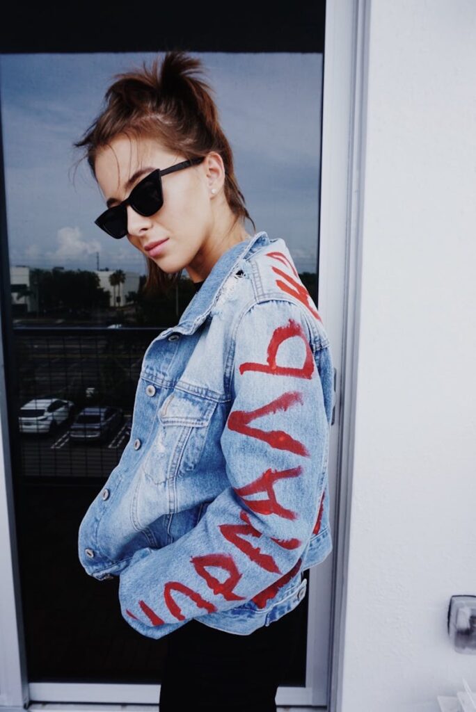 A fashionable woman poses confidently in a denim jacket outdoors.