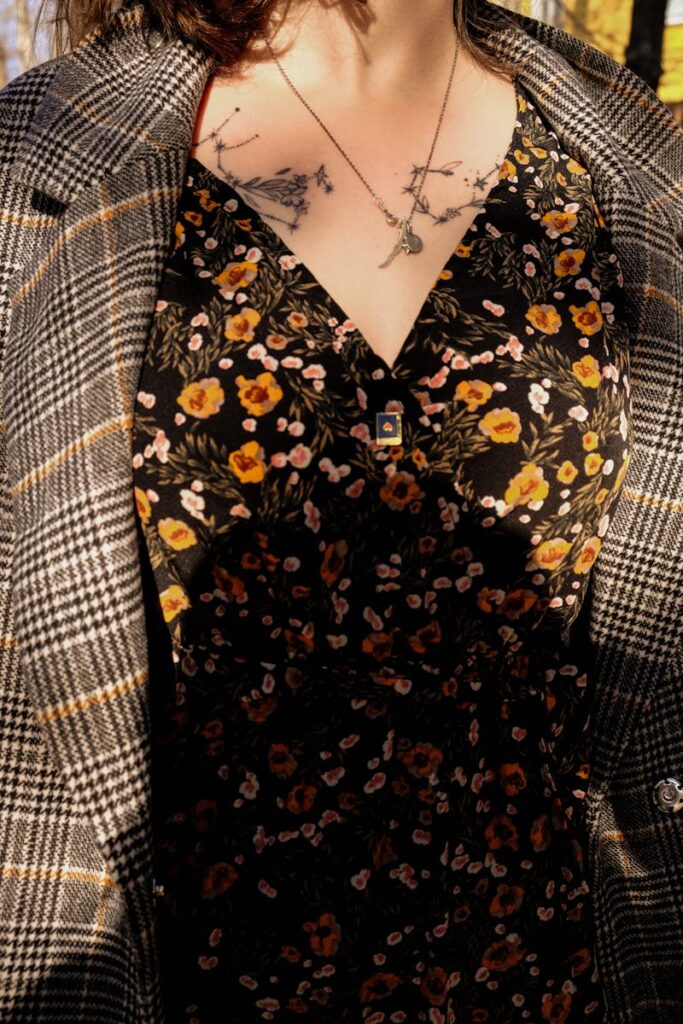 Close-up of woman wearing a floral dress and plaid jacket, showcasing floral tattoos and necklace.