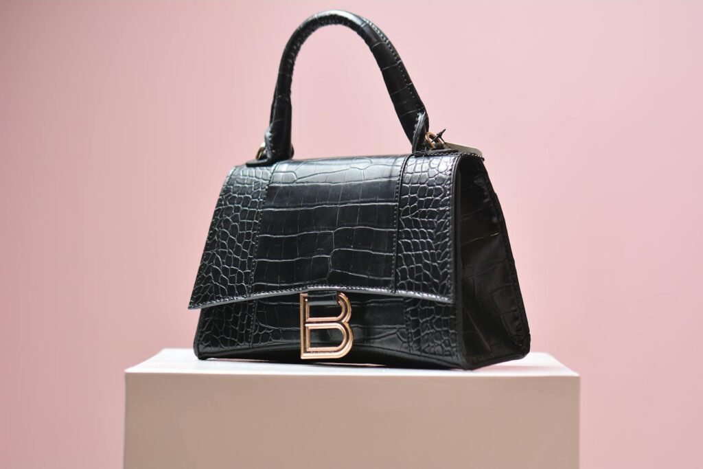 Elegant black leather handbag with textured design on a pink background, perfect for high-end fashion shoots.