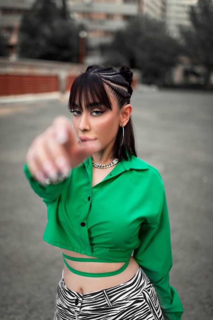 Stylish woman with bangs and braids in green crop top poses confidently outdoors, showcasing modern fashion.