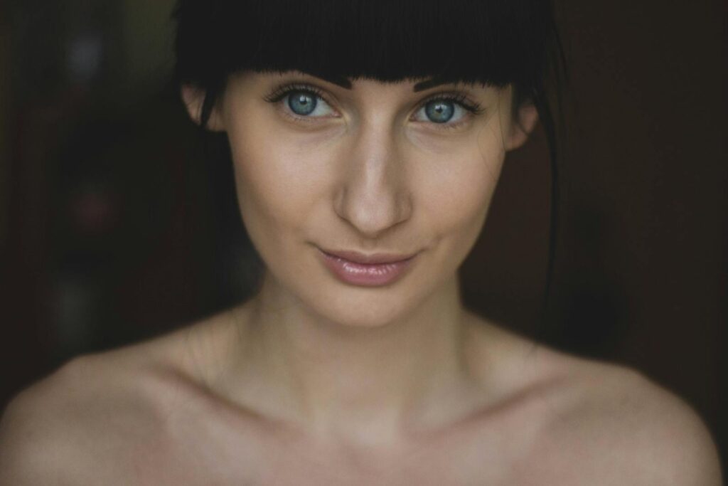 A close-up portrait of a woman with striking blue eyes and natural makeup, exuding confidence.