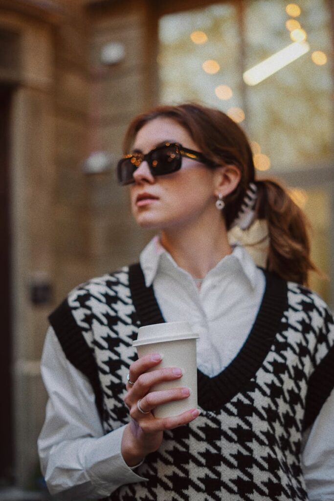 Stylish woman in sunglasses with coffee cup enjoying a sunny urban scene.