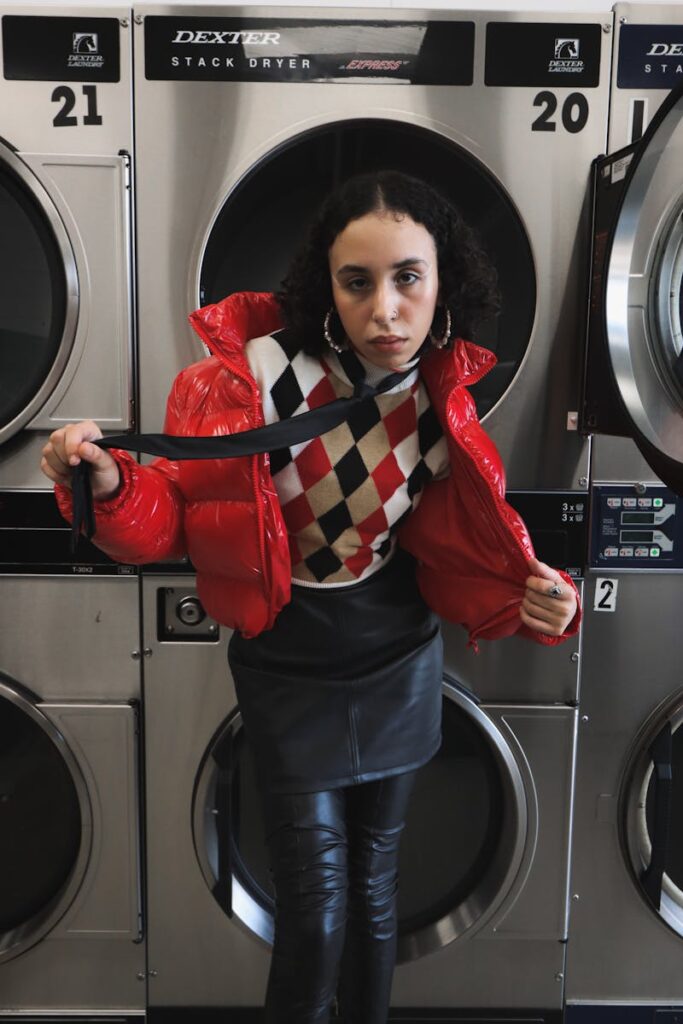 Stylish woman in laundromat wearing a bold red jacket and leather skirt.