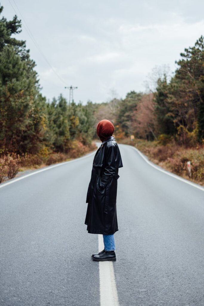 Person in black coat standing on an empty forest road, embodying solitude and fashion.
