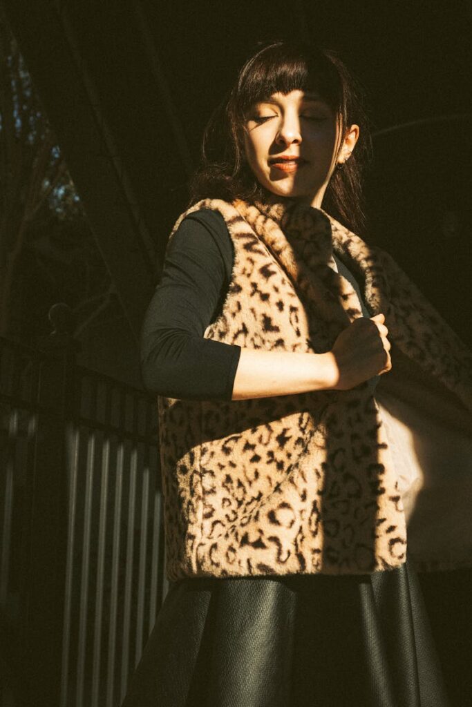 Fashionable woman in cheetah print vest enjoys sunlight in an outdoor setting.