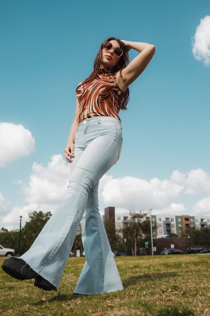 Fashionable woman in sunglasses and jeans posing confidently in a sunny outdoor setting.