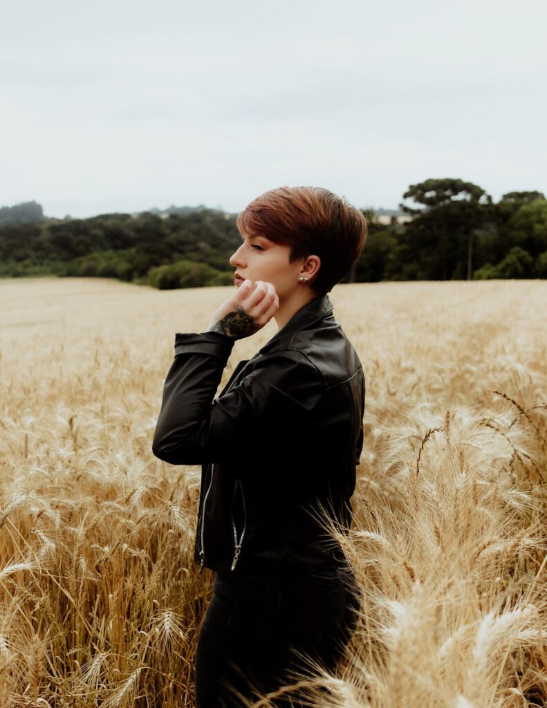 Profile of a stylish woman in a black leather jacket standing thoughtfully in a field of wheat.
