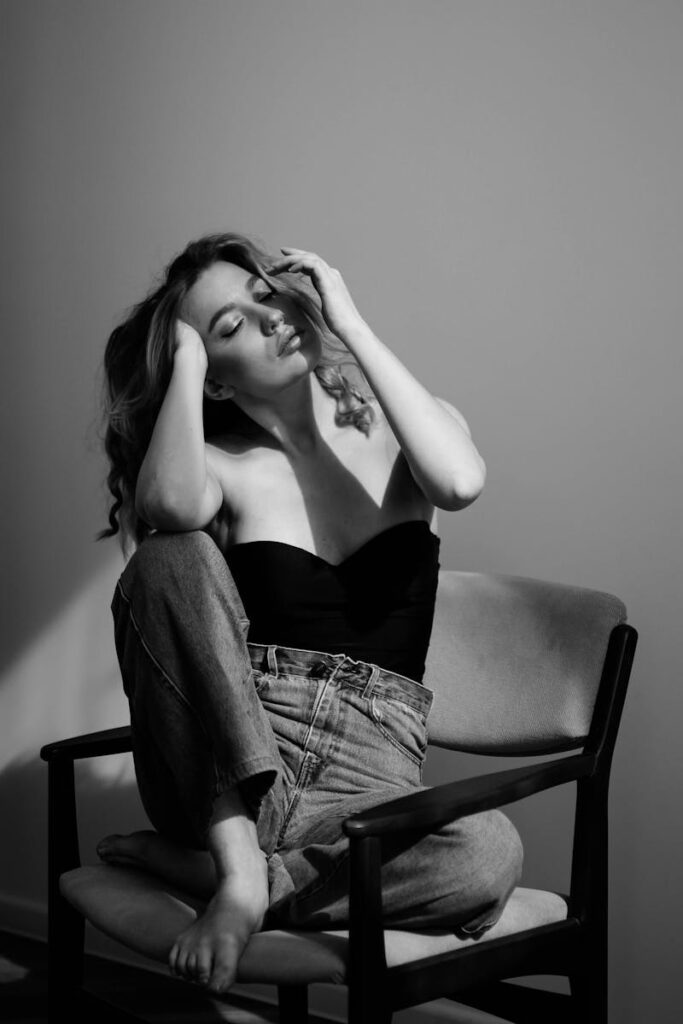 Black and white portrait of a woman wearing jeans and a bodysuit seated on a chair.
