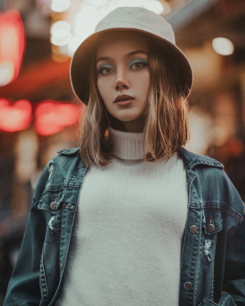 Fashionable portrait of a woman wearing a denim jacket and hat against an urban background.
