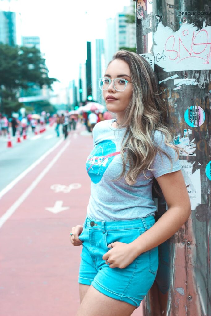 Fashionable woman in blue shorts and glasses posing on a vibrant street, showcasing urban style.