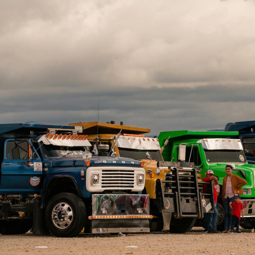 A row of vibrant trucks lined up outdoors with a family nearby under an overcast sky.