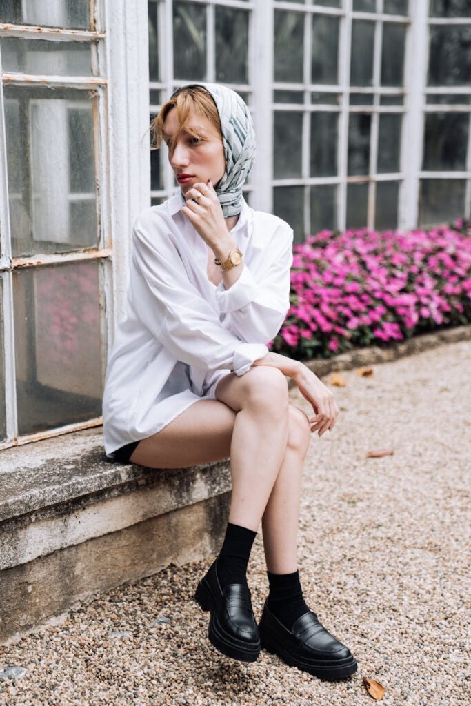 Stylish woman wearing a headscarf and sitting outside in a serene setting, exuding timeless fashion.