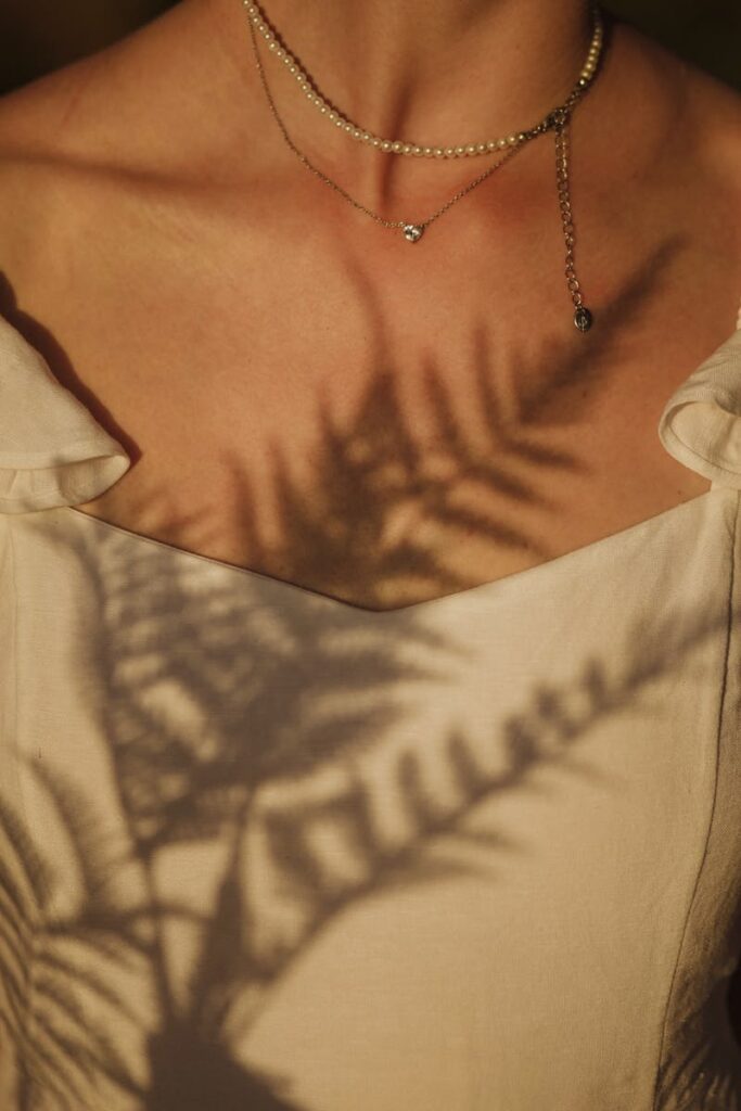 A close-up view of a woman wearing necklaces with fern shadows on her skin, creating an artistic effect.