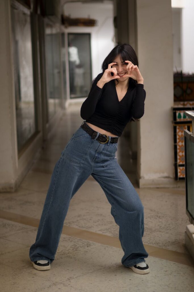 Joyful woman in casual attire playfully posing in an indoor corridor setting.