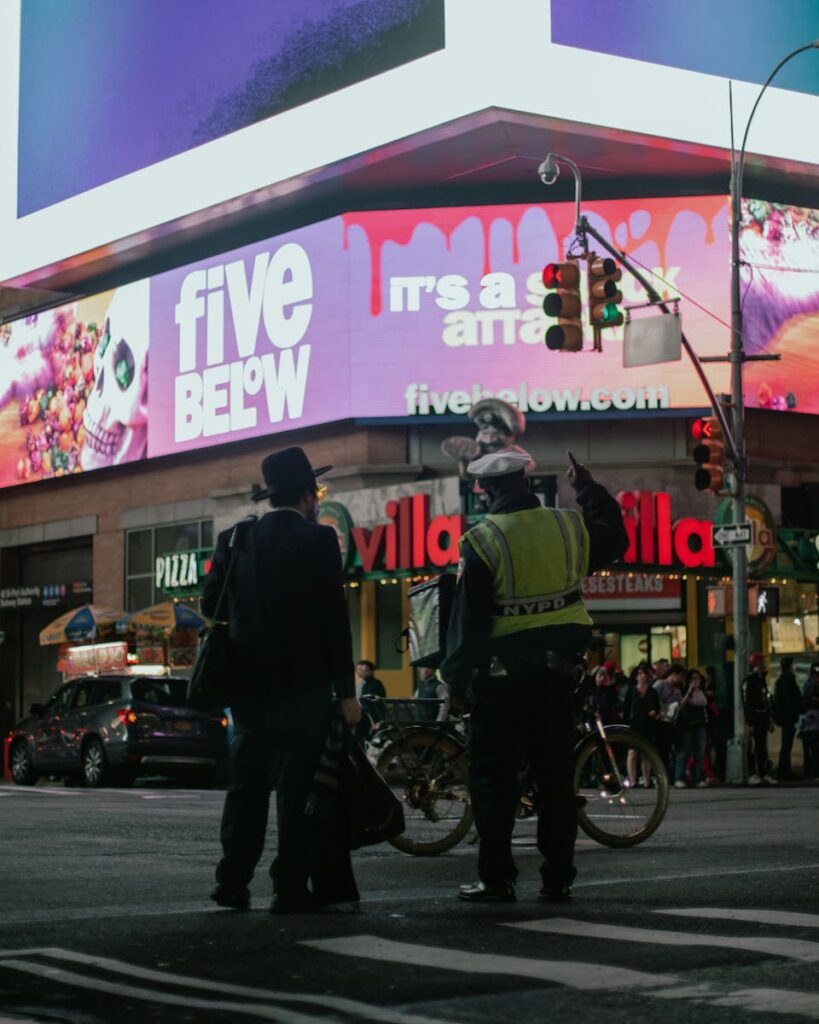 Bustling street scene in Times Square featuring pedestrians and a police officer at night.