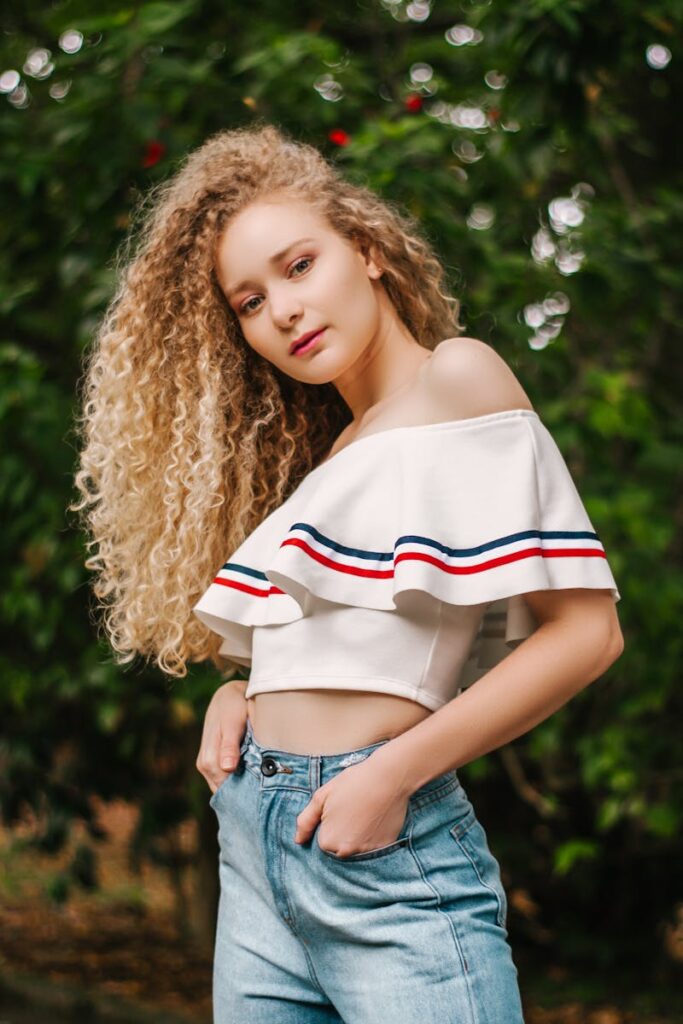 Stylish young woman with curly hair posing in denim outdoors.