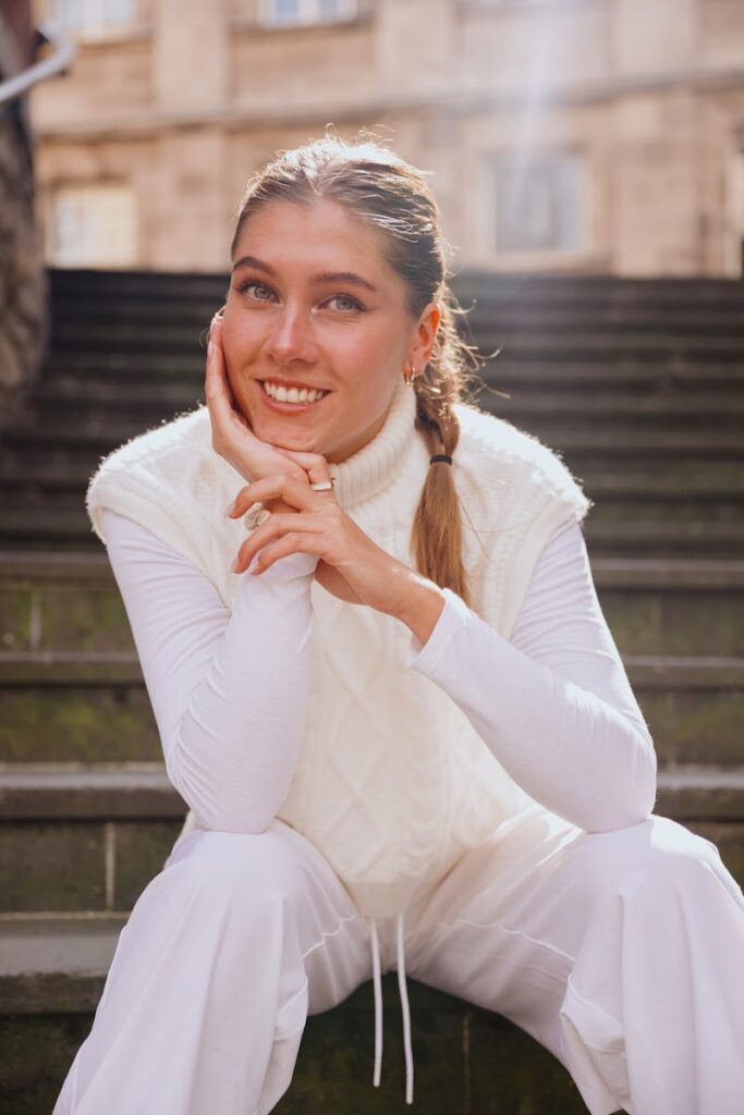 Smiling woman in white clothing sitting on outdoor stairs in Cologne, Germany.