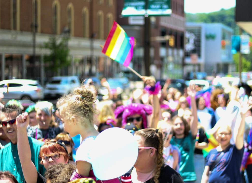 LGBTQ pride parade with multicolored flags and a lively crowd in a city street.